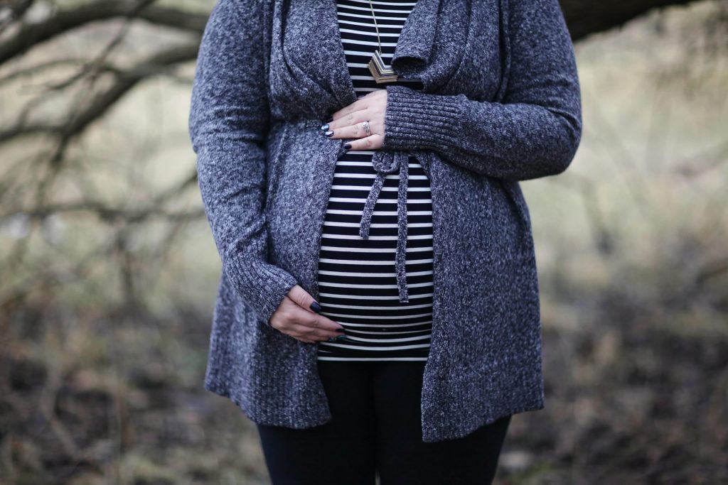 Pregnant woman in striped shirt and cozy sweater outdoors, embracing motherhood.